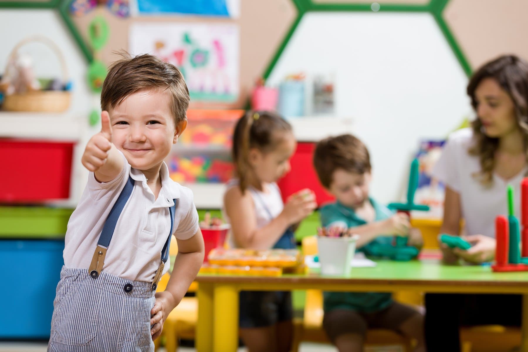 A happy child giving a thumbs up in a colourful daycare classroom